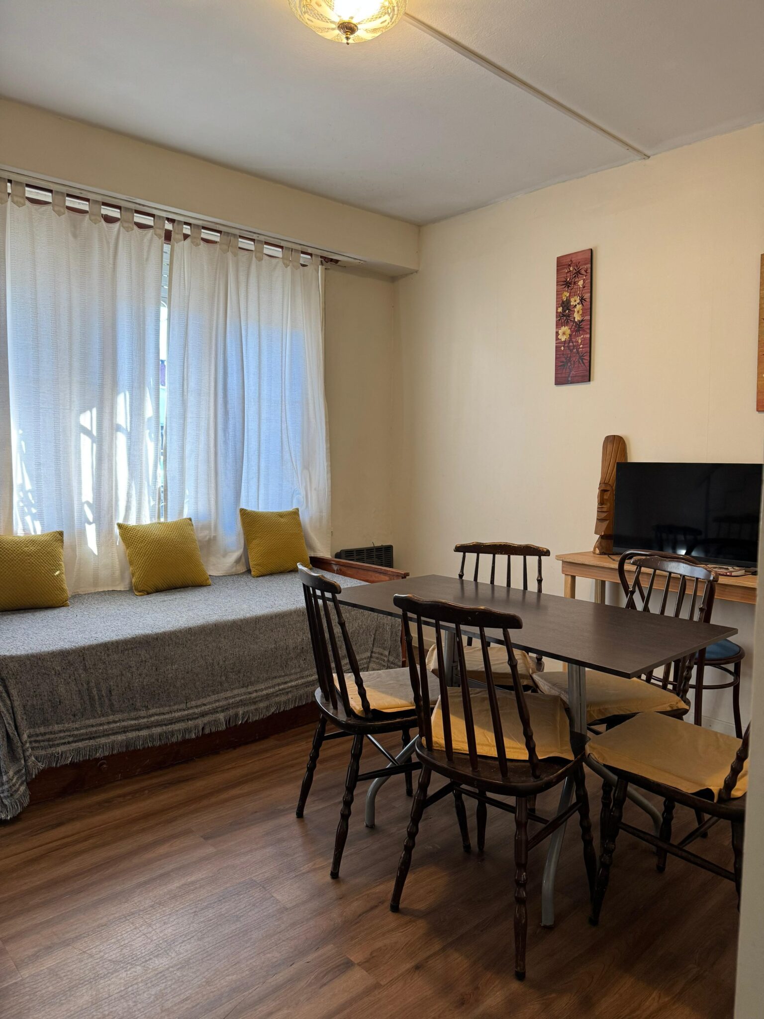 Primera vista de la cocina-comedor de Chauvín 1. Se muestra un sillón cama, una mesa para 6 personas, un ventanal, un televisor y una mesita